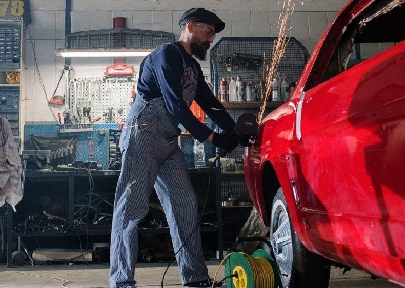 Technician grinding a part next to a red car