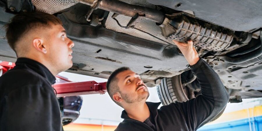 Two technicians inspecting the underside of a car